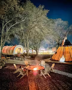 Conestoga glamping wagons and a teepee lit up at night around the fire pit at Splash RV Resort