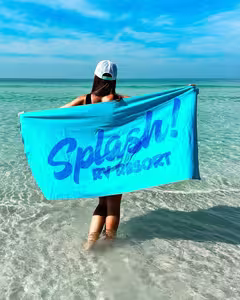 A guest on the Gulf Coast beach holding a Splash RV Resort towel near Pensacola, Florida
