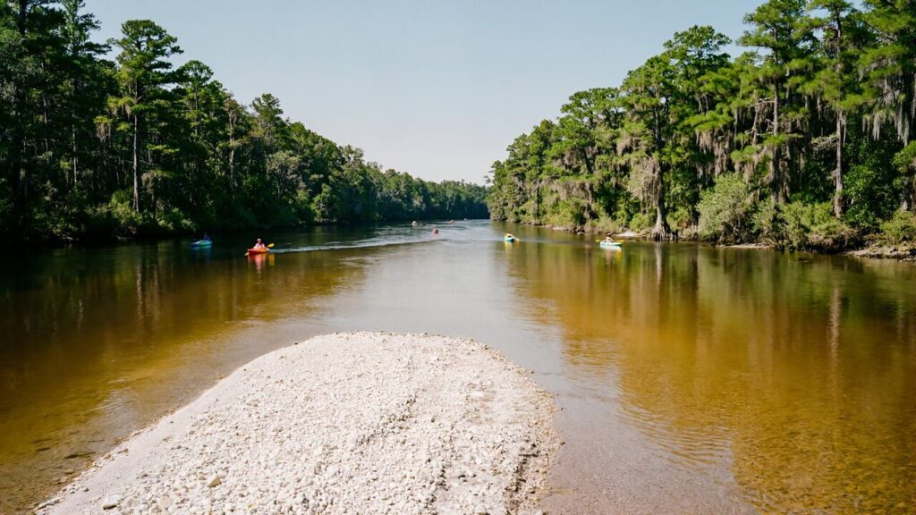 Kayakers and a tuber floating the clear, tannin-dark Blackwater River over bright white sandbars near Milton in Florida's Canoe Capital, a short drive from Splash RV Resort
