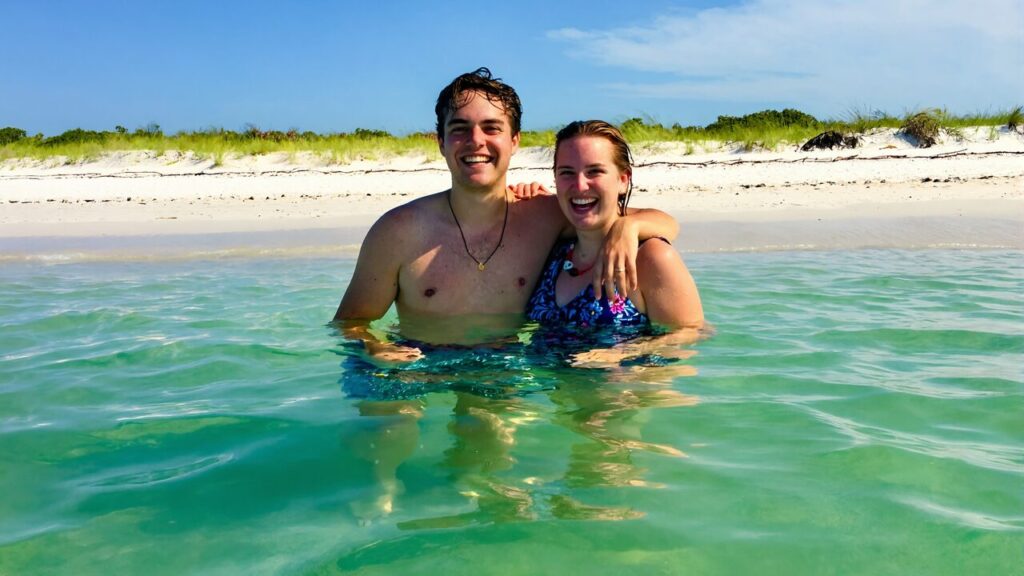 A young couple wading in the emerald-green Gulf water at a sugar-white sand beach on the Emerald Coast