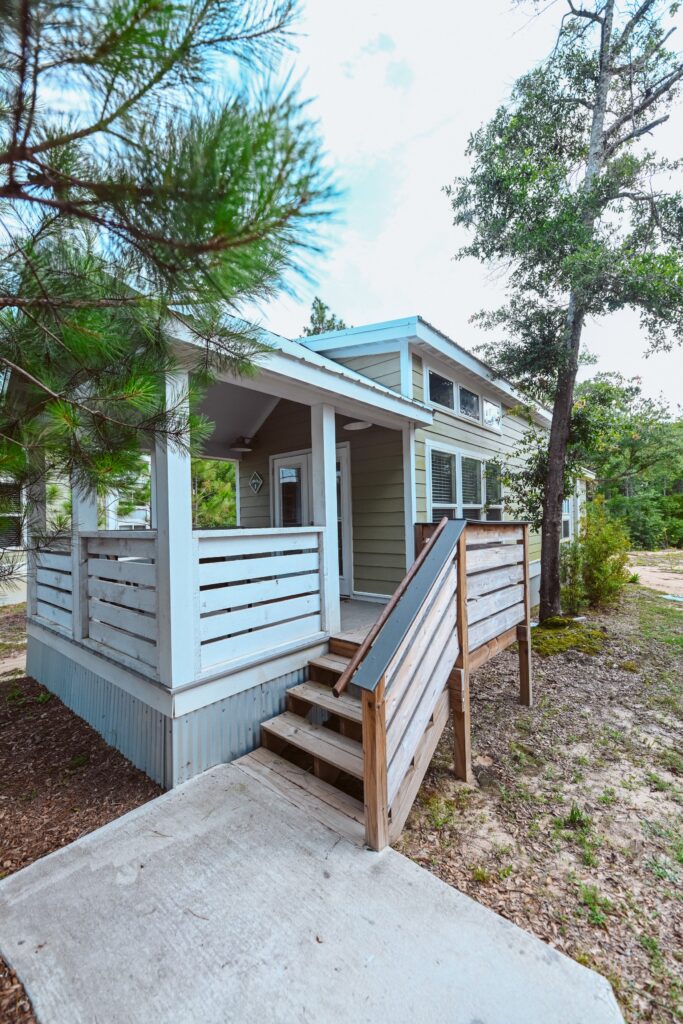Light green luxury cottage with covered porch and pine-tree surroundings at Splash RV Resort