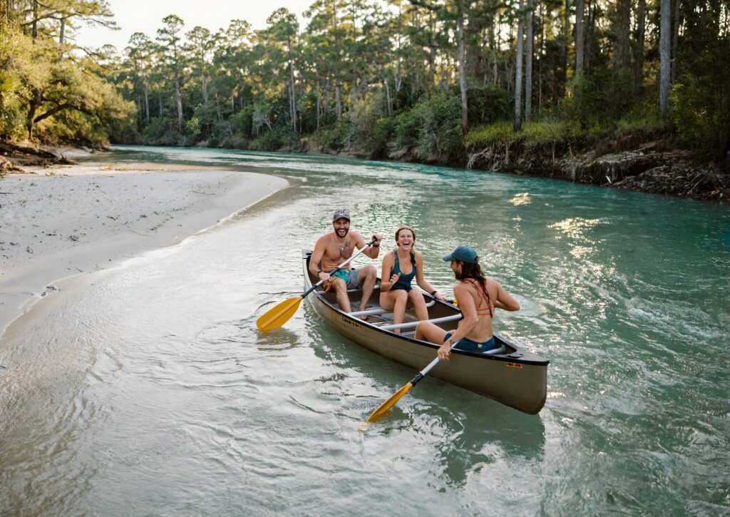Three friends paddling a canoe down the clear sandy bottomed Blackwater River lined with pine forest near Milton Florida