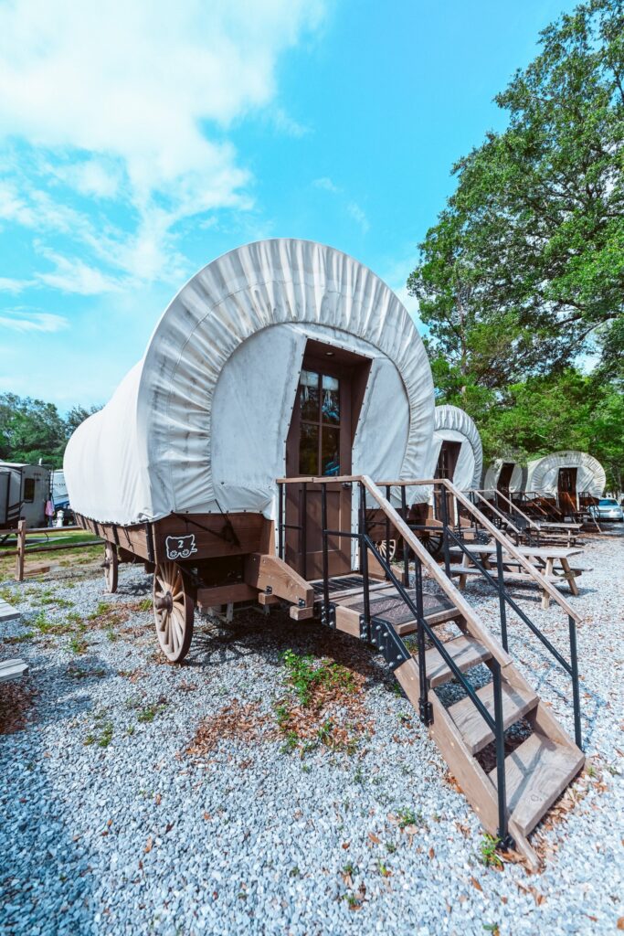 Conestoga-style covered glamping wagons with wooden steps on gravel pads at Splash RV Resort near Milton, Florida