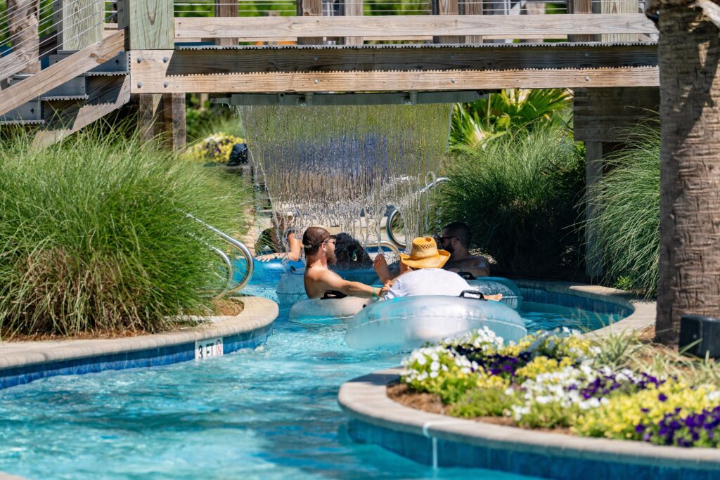 Guests floating on tubes down the lazy river under a waterfall feature at Splash RV Resort