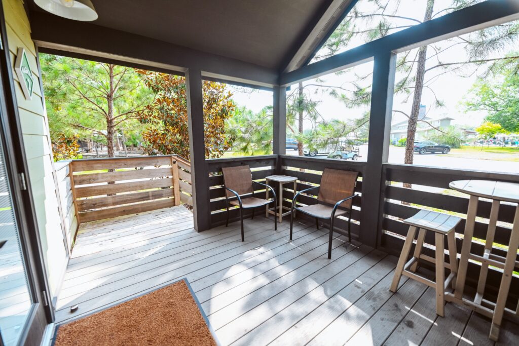 Sunlit screened porch of a luxury cottage at Splash RV Resort with comfortable chairs overlooking pine trees and the campground.