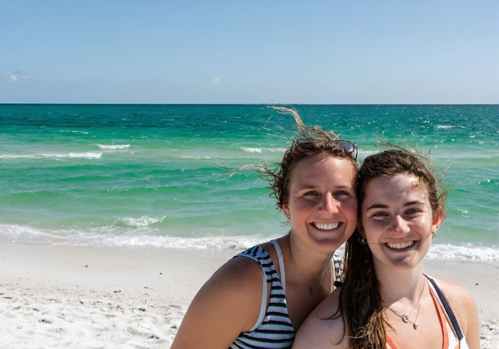 Two happy young women on the sugar-white sand and emerald water of a Gulf beach near Navarre Beach