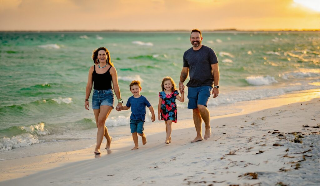 A family of four walking on the sugar-white sand at the emerald-green Gulf of Mexico at sunset