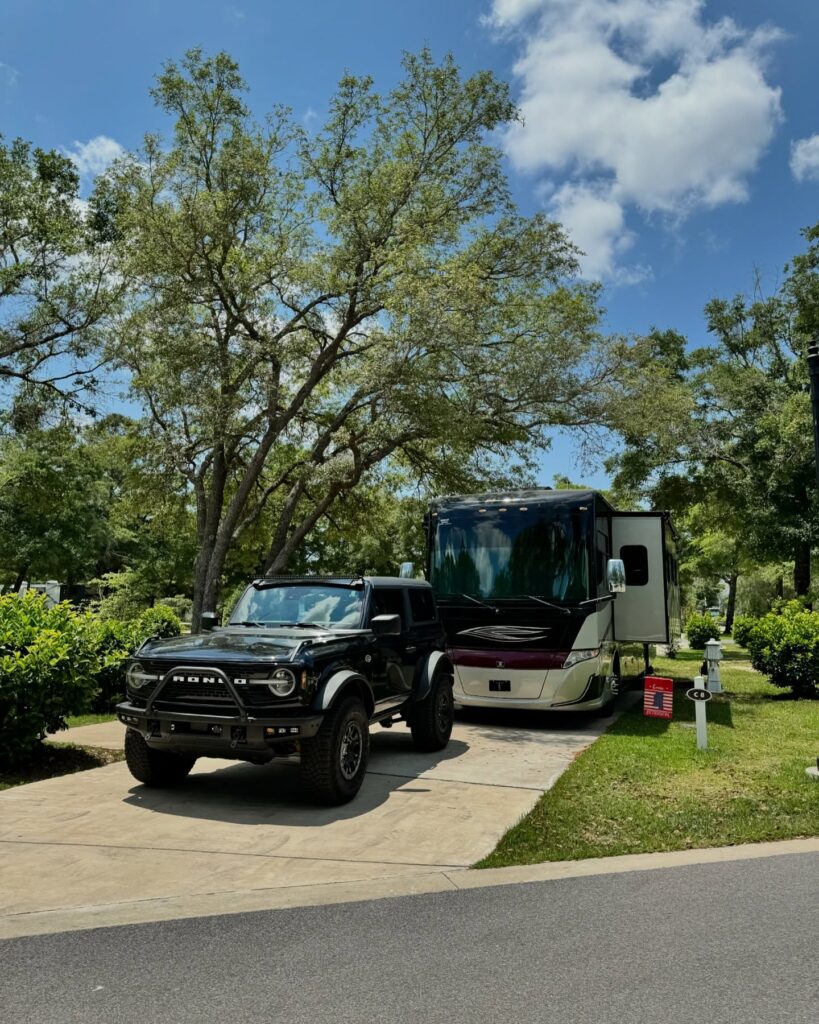 A motorhome and tow vehicle parked on a shaded concrete full hookup RV site at Splash RV Resort