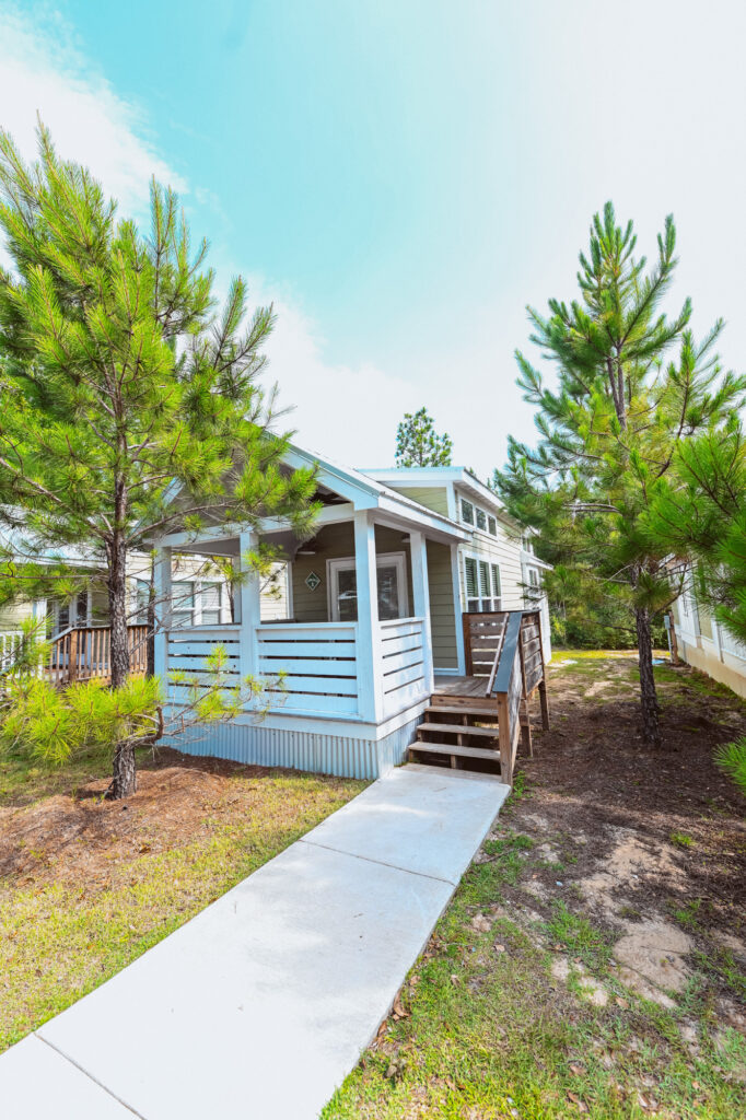 A light-blue luxury cottage with a covered porch among tall pines at Splash RV Resort near Pensacola, Florida