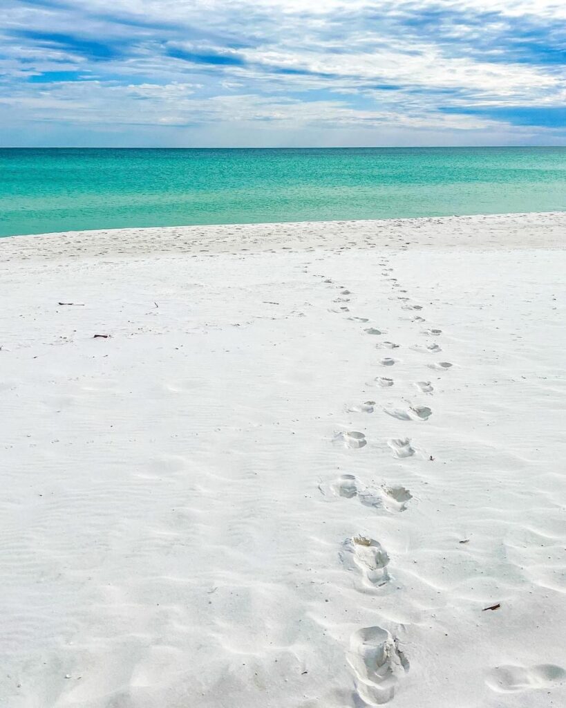 Footprints across white sand leading to emerald Gulf water at a beach near Splash RV Resort