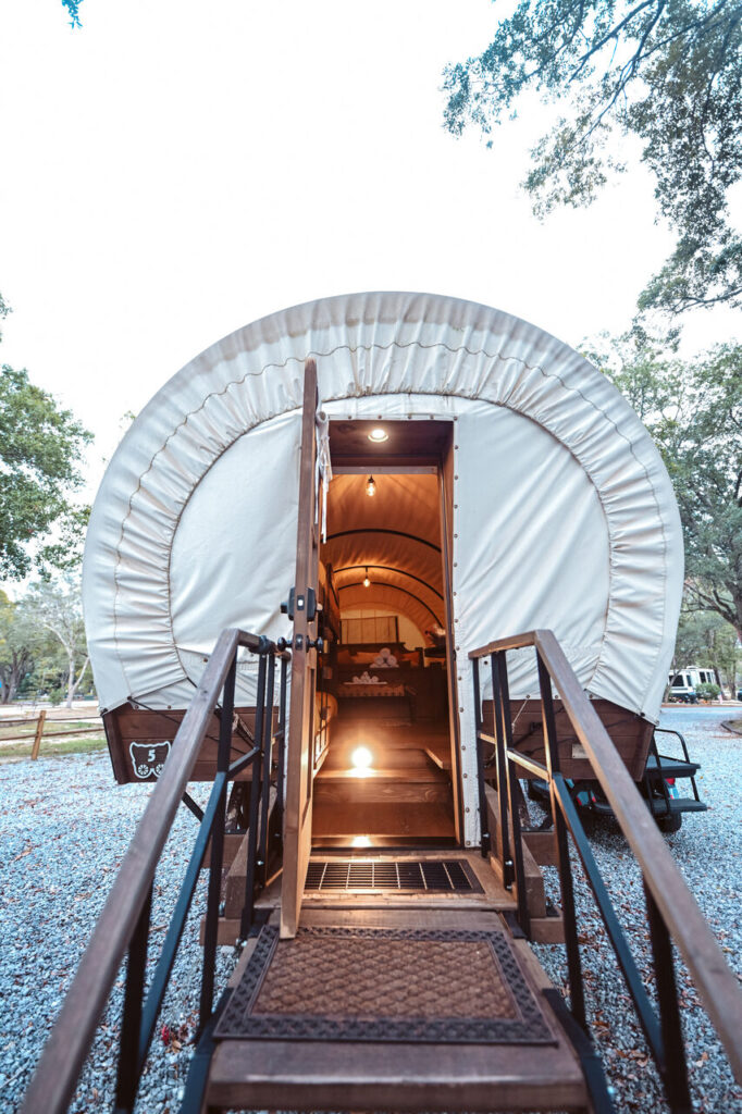 Wooden ramp with black railings leading into the open doorway of a canvas covered glamping wagon at a campground near Pensacola
