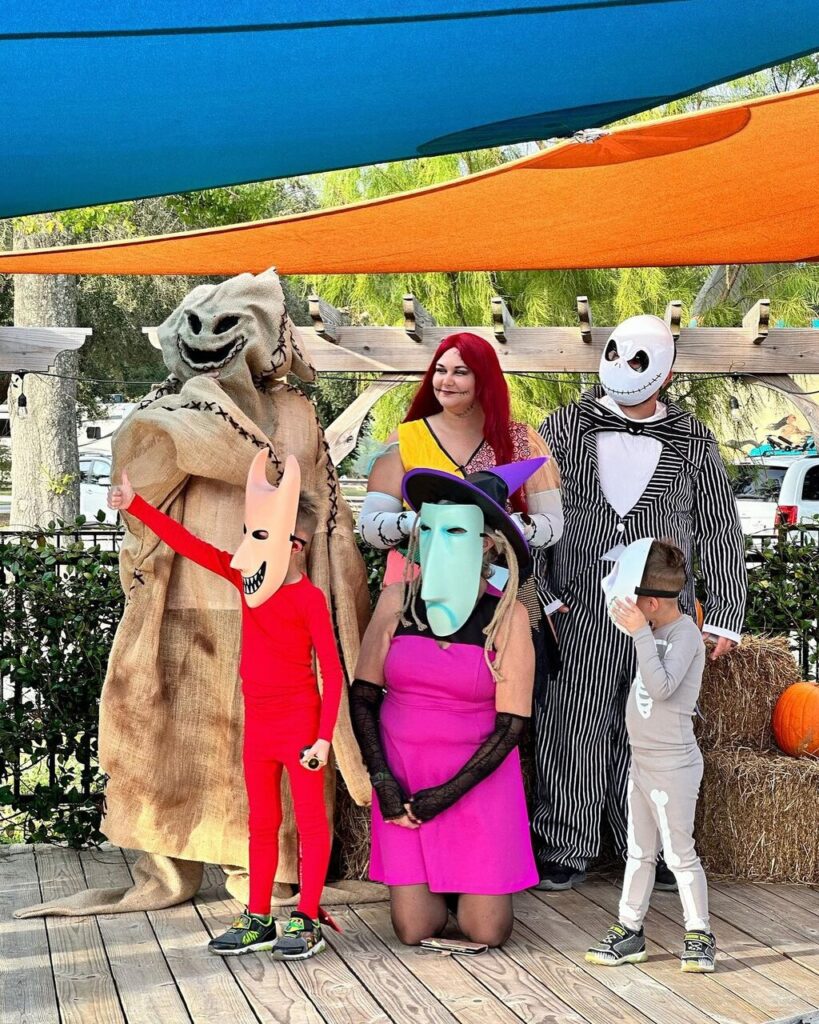 Guests in Halloween costumes posing on a wooden stage with hay bales and a pumpkin at Splash RV Resort near Pensacola Beach
