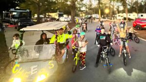 Kids on bicycles beside a decorated golf cart on a paved road past parked RVs at Splash RV Resort near Pensacola FL