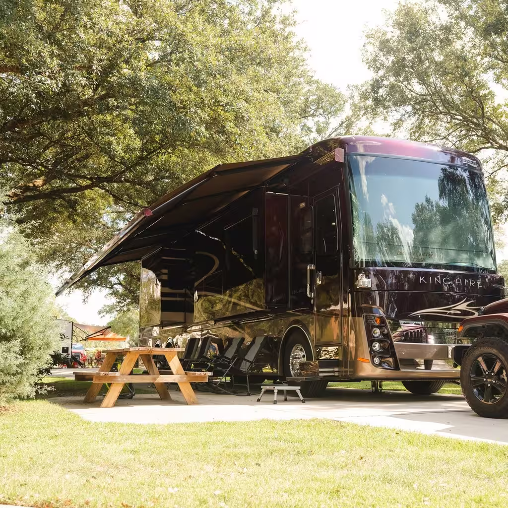 Large motorhome parked on a concrete pad with its awning out over a picnic table at an RV campground near Pensacola Florida