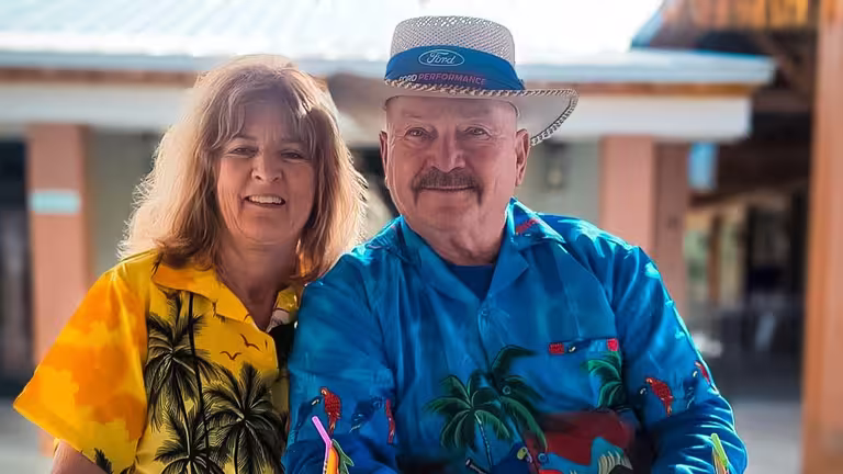 Two smiling guests in tropical print shirts on a sunny day at Splash RV Resort, one of the RV resorts in Florida near Pensacola