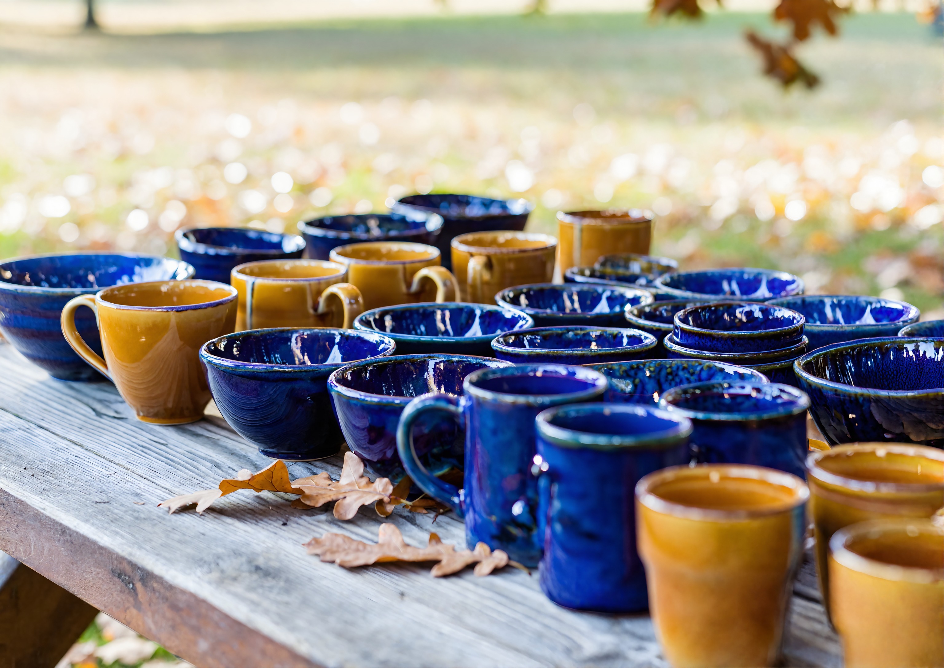 Handmade glazed pottery on a wooden table at an outdoor autumn arts festival near Pensacola, Florida