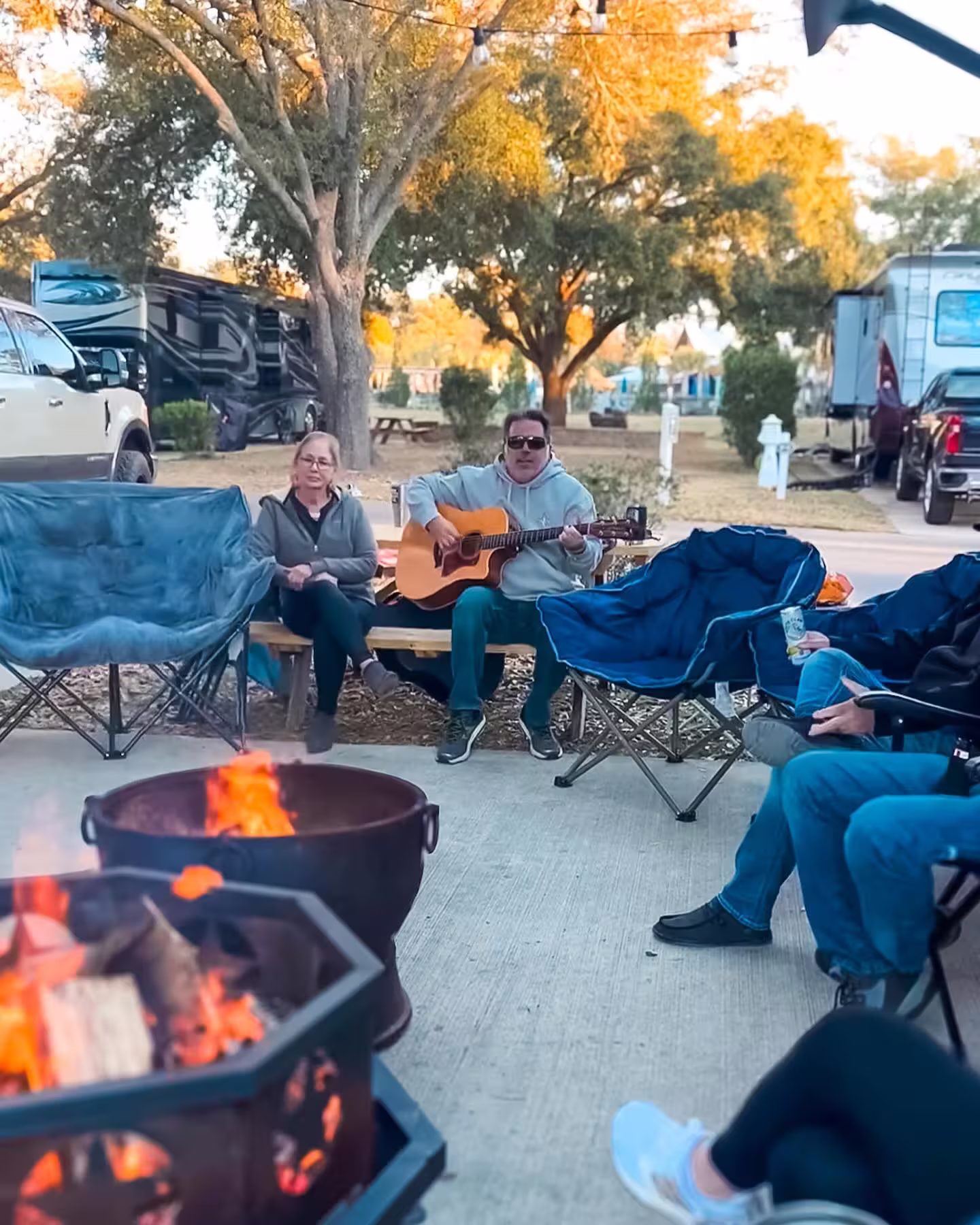 Campers in jackets around a fire pit with live guitar at an RV resort near Pensacola, Florida