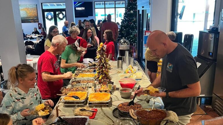 Guests fill their plates at a long holiday potluck buffet beside a decorated Christmas tree at Splash RV Resort, an extended stay option near Pensacola, Florida