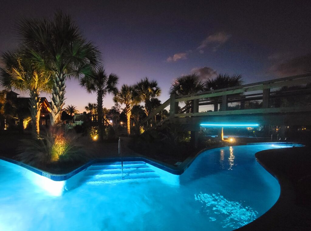 The lazy river at Splash RV Resort in Milton, FL, lit up bright blue at dusk under palm trees