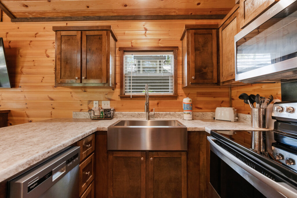 Full kitchen with a stainless farmhouse sink, dishwasher and wood cabinets inside a luxury cottage at Splash RV Resort near Pensacola