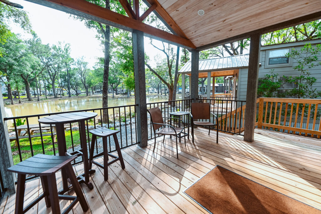 Covered front porch of a luxury cottage rental at Splash RV Resort near Pensacola, with a high-top table, stools and patio chairs looking out over a pond and lawn