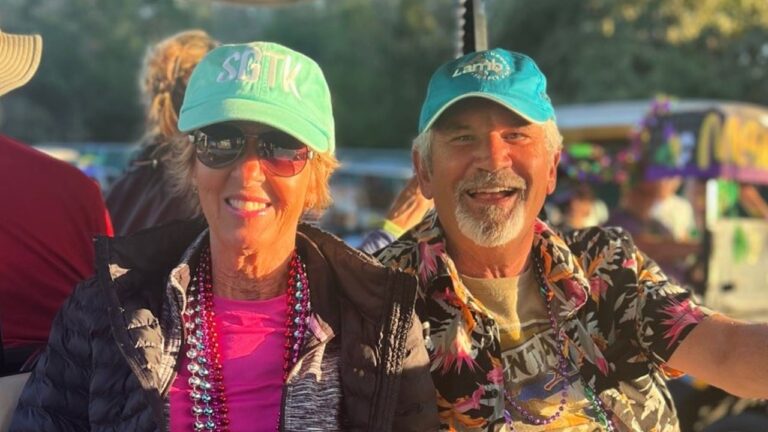 Smiling older couple in ball caps and purple and green Mardi Gras beads riding in a golf cart during a holiday event at Splash RV Resort, a snowbird rental near Pensacola, Florida