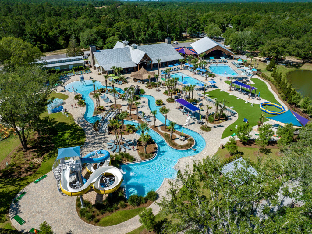 Aerial view of Splash RV Resort near Pensacola showing the winding lazy river, yellow and blue water slides, several pools and palm trees surrounded by pine forest
