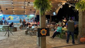 Guests relax at picnic tables under string lights in the Splash RV Resort pavilion, a home base for day trips to Orange Beach AL