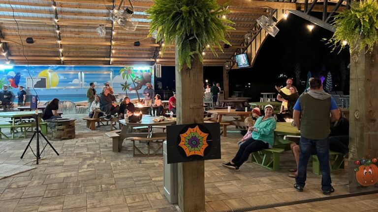 Guests relax at picnic tables under string lights in the Splash RV Resort pavilion, a home base for day trips to Orange Beach AL