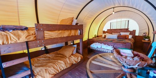 Glamping wagon interior with wooden bunk beds and queen bed under arched canvas canopy at Splash RV Resort in Milton, Florida.