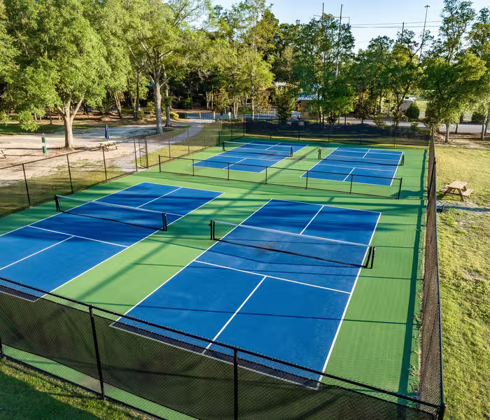 Aerial view of four blue pickleball courts at Splash RV Resort surrounded by green surfacing and trees.