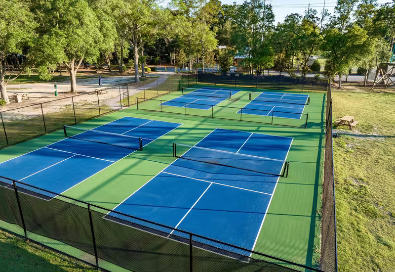 Aerial view of four blue pickleball courts at Splash RV Resort surrounded by green surfacing and trees.