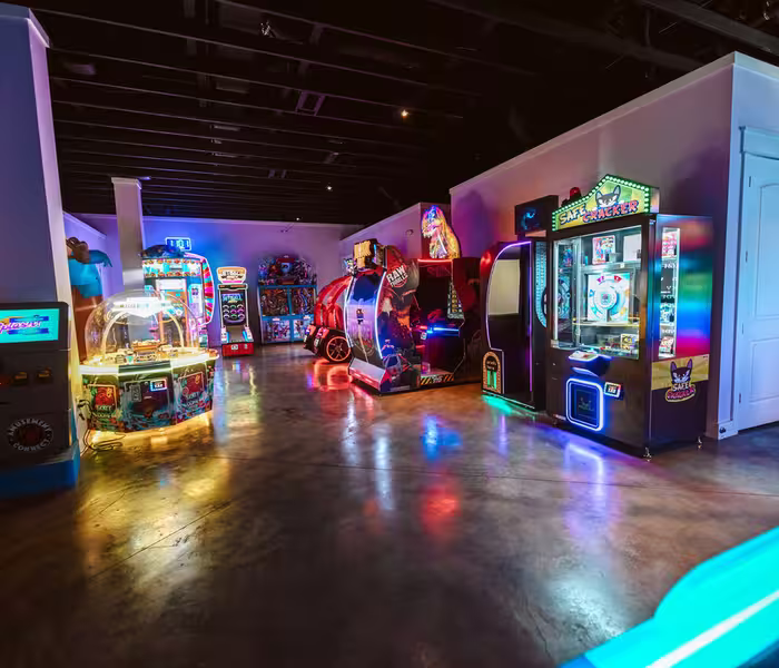 Indoor arcade at Splash RV Resort featuring neon-lit game machines and ride-on attractions on a polished concrete floor.