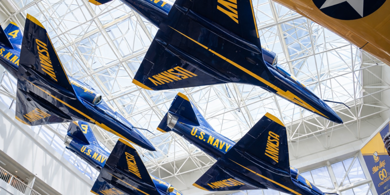 Four blue and yellow U.S. Navy Blue Angels jets suspended in diamond formation from the ceiling of a museum atrium with glass-paneled geometric roof and natural light at Splash RV Resort in Milton, Florida.
