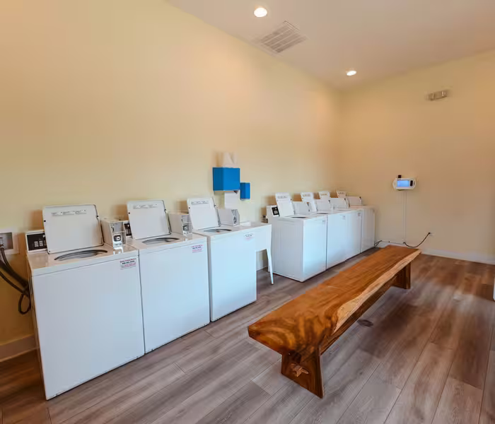 Bright laundry room at Splash RV Resort with white machines and a wooden bench.