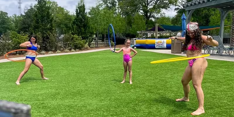 Guests playing with hula hoops on the green lawn at Splash RV Resort near the water playground.