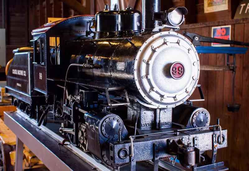 Detailed miniature steam locomotive numbered 99 on display tracks inside a wooden building at Splash RV Resort.