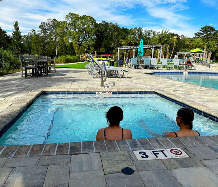 Two women relaxing in the bubbling hot tub at Splash RV Resort, surrounded by a paver deck and lounge chairs.