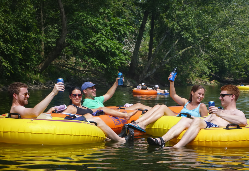 Guests toasting on yellow tubes in the Splash RV Resort lazy river, surrounded by lush green trees and calm water.