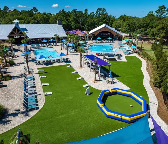 Aerial view of Splash RV Resort swimming pools surrounded by lounge chairs and umbrellas with cornhole games and gaga ball pit