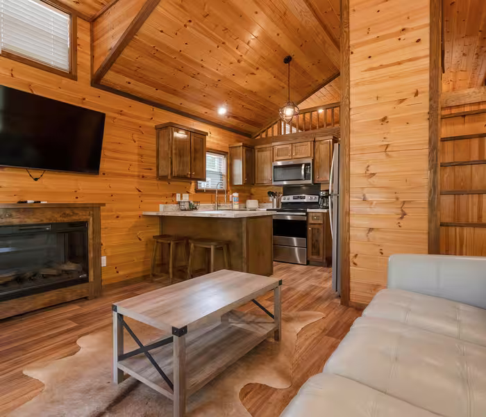 Luxury cottage interior with honey-toned pine walls, cream leather sofa, and electric fireplace at Splash RV Resort in Milton, Florida.