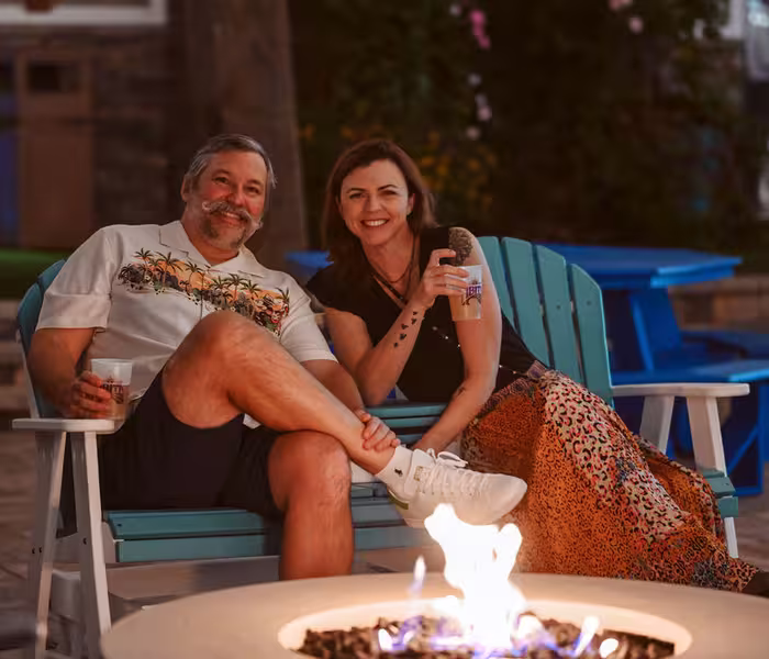 A couple relaxes on a turquoise Adirondack chair beside a modern concrete gas fire pit at Splash RV Resort in Milton