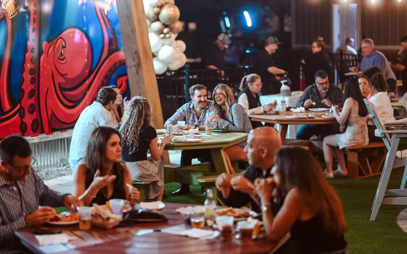 Guests share food and drinks at evening gathering with octopus mural at Splash RV Resort in Milton, Florida