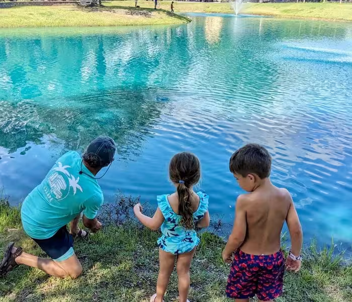 A family feeding fish by a turquoise pond fountain at Splash RV Resort in Milton, Florida