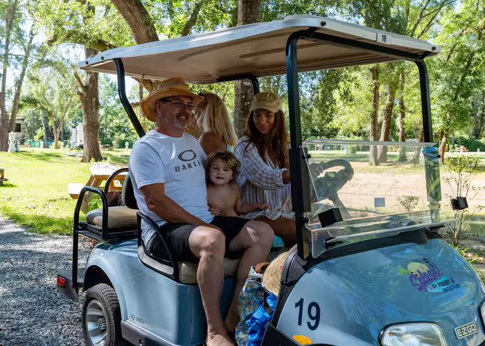 Family of four riding in a light blue golf cart at Splash RV Resort with trees and RVs in the background