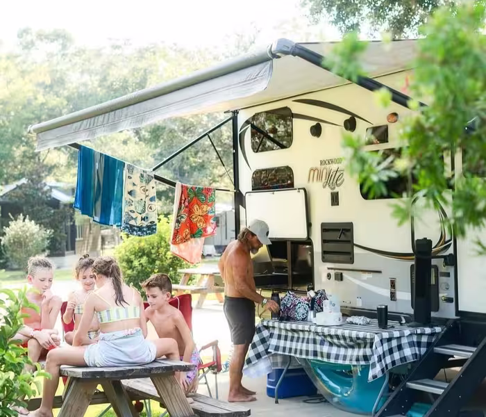 Family grilling and relaxing at their RV site with a picnic table under the awning at Splash RV Resort.