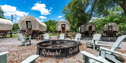 Glamping wagons parked near a fire pit with chairs at Splash RV Resort in Milton.