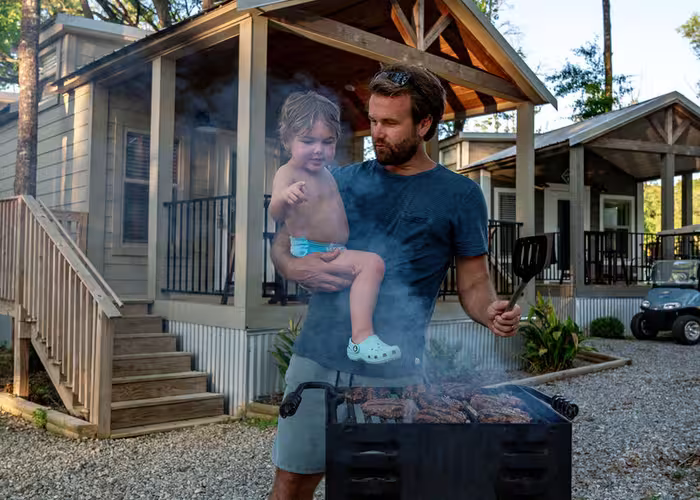 Bearded father holding toddler while grilling burgers at luxury cottage at Splash RV Resort in Milton, Florida