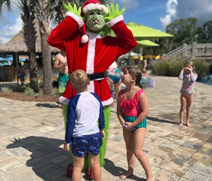 Grinch character in Santa suit greeting children on the paved patio at Splash RV Resort.