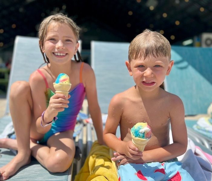 Two children holding rainbow-swirled ice cream cones by poolside lounge chairs at Splash RV Resort in Milton, Florida